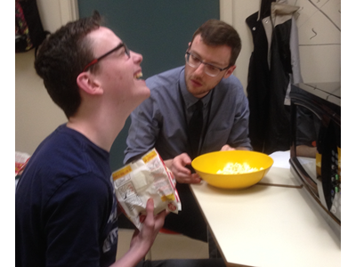 Images shows a student laughing while pouring a bowl of popped popcorn