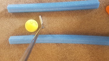 A foam ball situated between two pool noodles. A golf putter is poised to hit the ball.