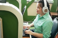 A person sits at a computer wearing headphones and typing on a keyboard.